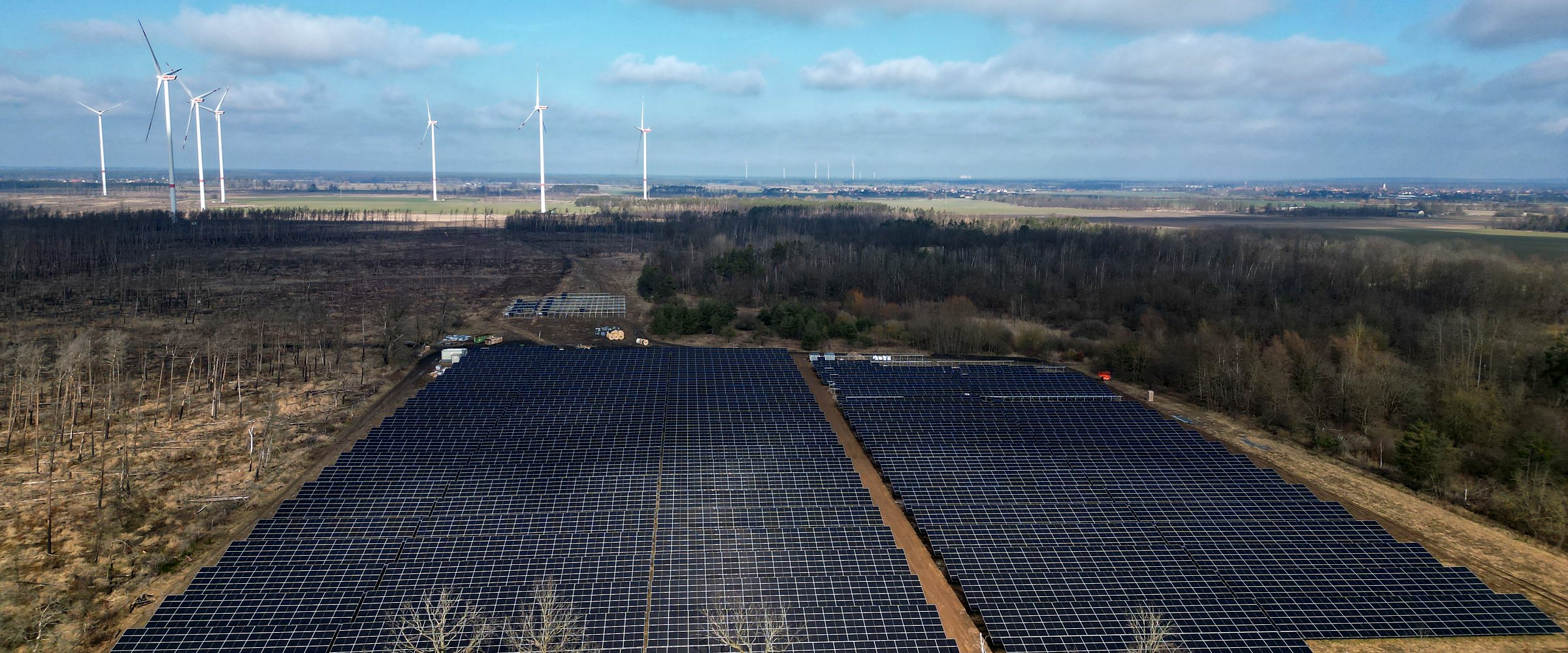 Luftaufnahme der Photovoltaik-Freiflächenanlage Falkenberg in Brandenburg, im Hintergrund Windräder