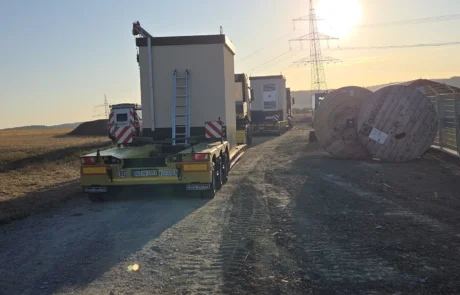 Anlieferung der Übergabestationen auf Tiefladern bei Sonnenaufgang an der Baustellenzufahrt, Solarpark Mulfingen, Hohenlohekreis