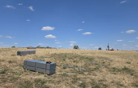 Gebündelte Rammpfosten aus Stahl-C-Profil auf dem abgesteckten Baufeld, Rammgerät im Hintergrund, PV-Freiflächenanlage Mulfingen I, Hohenlohekreis
