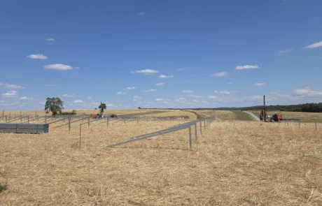 Erste Reihen gerammter Stahlpfosten mit Rammgerät und Pfostenbündeln, Baufeld Solarpark Mulfingen, Hohenlohekreis