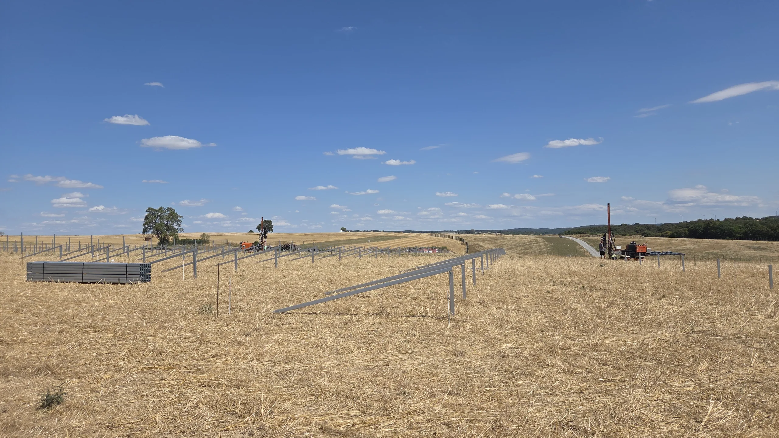 Rammarbeiten Solarpark Mulfingen Erste Reihen gerammter Stahlpfosten mit Rammgerät und Pfostenbündeln, Baufeld Solarpark Mulfingen, Hohenlohekreis